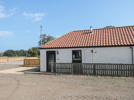 The exterior of a single-story house with a tiled roof a wooden fence and a gravel driveway at Curlew Cottage near Filey