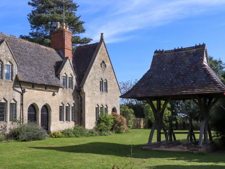 A stone house with a tiled roof and black windows next to a wooden structure with a tiled roof in a garden at The Alms House East in Forthampton near Tewkesbury