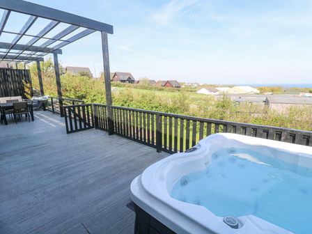 An outdoor deck with a hot tub table and chairs with houses and greenery in the background at Bay View in Portreath