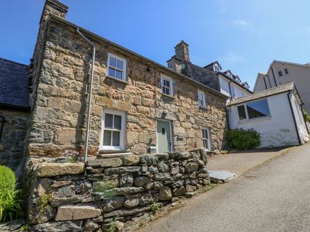 A stone exterior cottage with windows a door and a stone wall next to a paved driveway at Caereinion in Harlech