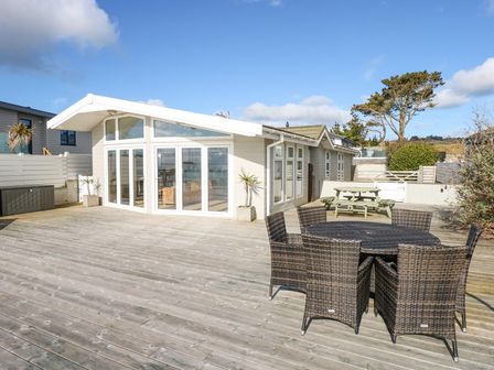 An outdoor wooden deck with wicker chairs around a table and a wooden picnic table near a building at The Warren M45 in Abersoch