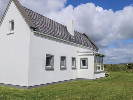 The exterior of a white house with multiple windows and a grass lawn at No 3 Beach Cottages in Keel County Mayo