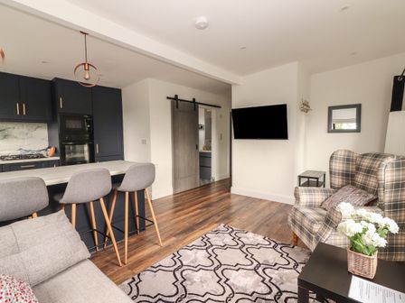 An open living area with a kitchen island and bar stools a plaid armchair and a mounted TV at Hogans Cottage Cullenagh near Ennistymon County Clare