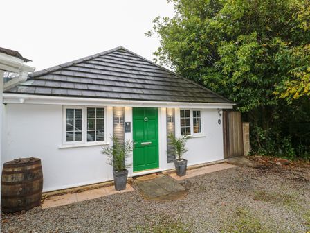 A white cottage with a green door two potted plants gravel driveway and a wooden barrel at Dowager Cottage in Penryn