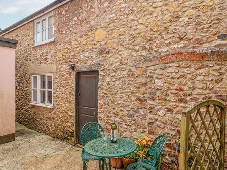 Stone walled courtyard with green metal table and chairs and potted flowers at Upside Down Cottage in Colyton