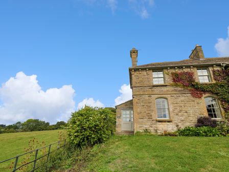 A stone house with ivy on the wall next to a grassy field under a blue sky at Ivy Cottage in Colerne