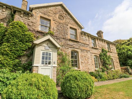 A stone cottage with green bushes and plants around the entrance at Blue Bell in Colerne