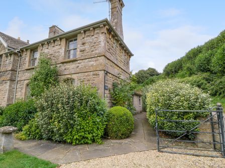 Stone house with a chimney surrounded by bushes and a metal gate at Peartree in Colerne