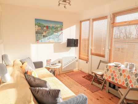 A living room with a sofa, cushions, a small table, a wall-mounted tv, wooden blinds on windows, and a dining table with chairs at 418 Norton Park in Dartmouth