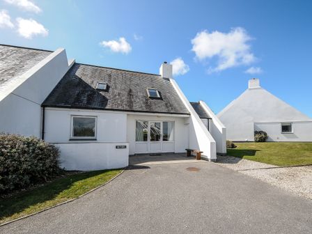 A white house with a sloped roof and skylights a driveway and a bench at Bryher in Trebetherick near Polzeath