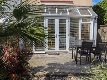A patio area with a wooden deck table and chairs and glass doors with blinds at Shepherds Walk in Duncannon County Wexford