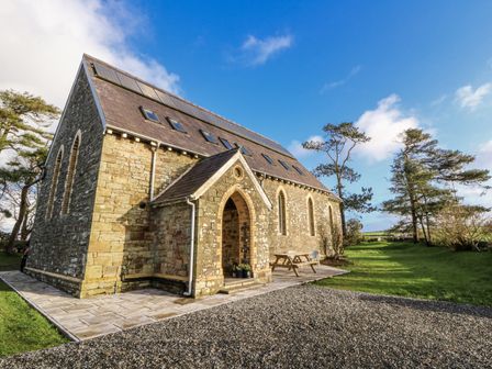 A stone building with solar panels and a patio at Church Llygad Y Dyffryn in Sarnau near Brynhoffnant