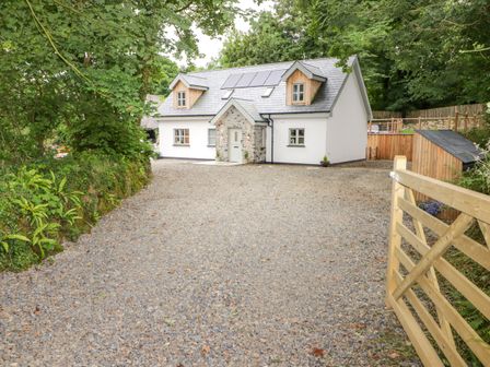 A gravel driveway leading to a house with dormer windows and solar panels surrounded by trees at The Grove in Wolfsdale near Haverfordwest