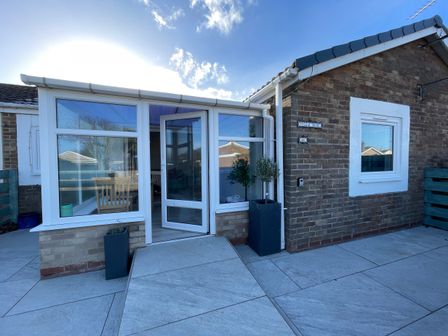 Front entrance of a brick house with a white framed glass porch and two potted plants on either side of the door at Villa Rose Beadnell near Seahouses