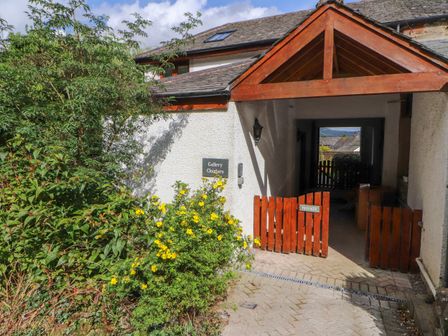 A building entrance with a wooden gate and flower bushes at Gallery Cloisters Thornthwaite near Keswick