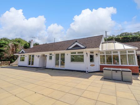 The exterior of a single story house with a tiled roof and a conservatory next to a paved patio at The Willows in Llangollen