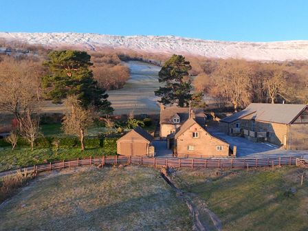 A country farmhouse with outbuildings surrounded by fields and trees with a snow-covered hill in the background at White Haywood Farmhouse in Craswall