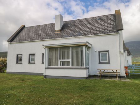 A white house with a gray roof and chimney with several windows and a picnic table on the lawn at No 5 Beach Cottages in Keel County Mayo