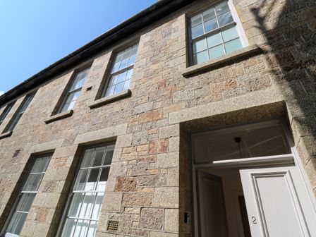 Stone exterior of a building with multiple windows and an open door showing number 2 at 2 Regent Mews in Penzance