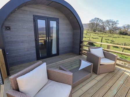 A wooden deck with two cushioned chairs and a small table outside a curved cabin at Shepherds View in Castlerigg near Keswick