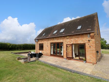 An exterior view of a brick house with patio furniture on a paved area and grassy lawn at Little Acre in Church Lench near Harvington