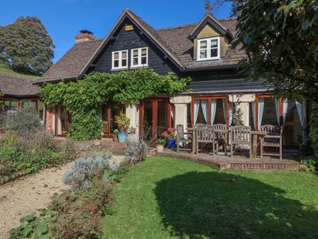 A house with a garden patio and outdoor wooden table and chairs at Highgrove Barn in Painswick