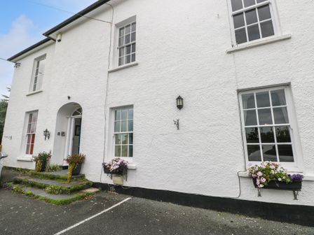 The front exterior of a white building with steps leading to a door and flower boxes under windows at Bay View Apartment in Penally near Tenby