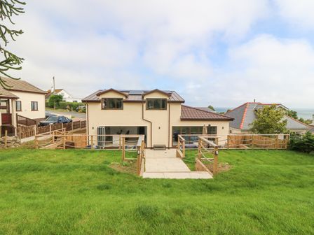 The rear view of a two-story house with a large grassy garden and wooden railing at The Bay in Benllech