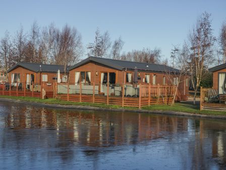 Wooden lodges with outdoor seating beside a frozen pond at The Three Bears Lodge Coniston Drive 11 South Lakeland Leisure Village near Warton