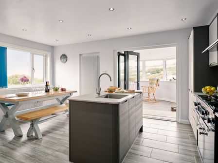 A kitchen with an island sink wooden dining table with bench and rocking chair in adjacent room at Carousel in Broad Haven