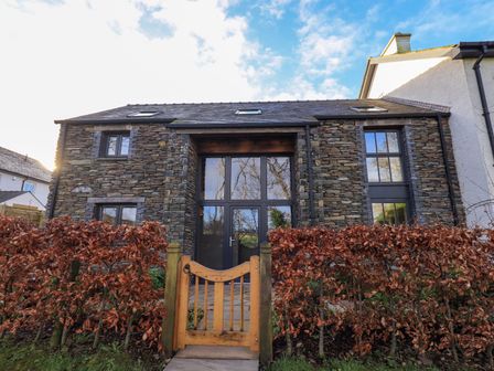 Stone house exterior with large windows and wooden gate in front at The Elterwater Barn in Lamplugh