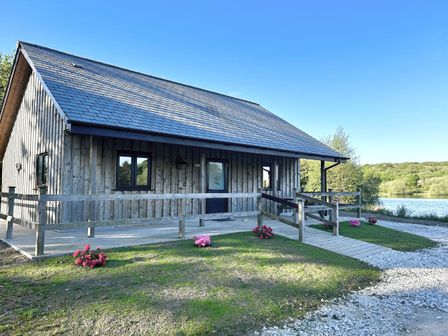 A wooden lodge with a deck and flowers outside at Kingfisher Lodge in Treverbyn near St Austell