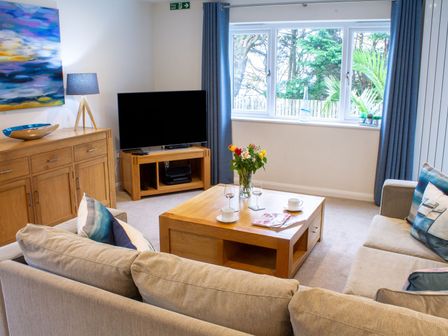 A living room with two sofas a wooden coffee table TV and cabinet at Sea Bleu in Carbis Bay