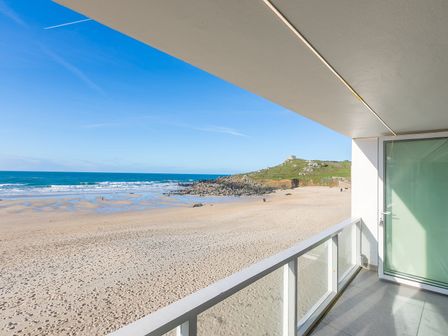 A balcony overlooking a sandy beach and ocean with a rocky hill in the background at Louies Loft in St Ives