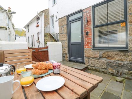 An outdoor wooden table with croissants orange juice and jam outside a stone and brick house at 2A Salubrious Terrace in St Ives