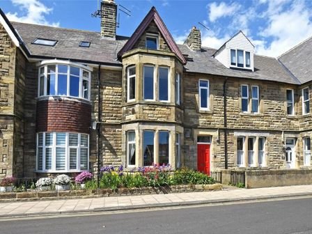 A stone terraced house with bay windows and a red door with flowers in front at Claremount in Alnmouth