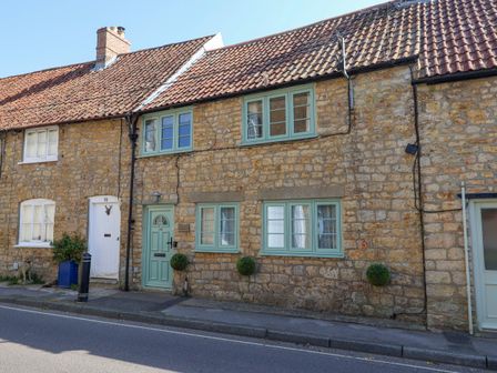 A stone cottage with green window frames and door with small plants outside on a street at 30 Fleet Street in Beaminster