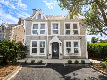 A two-story house with multiple windows a black front door and a paved driveway with plants at Highways in Morfa Nefyn