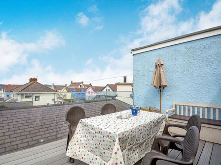 A rooftop patio with a table covered with a polka dot tablecloth surrounded by four chairs and a bench near a blue wall at Victoria House in Rhosneigr
