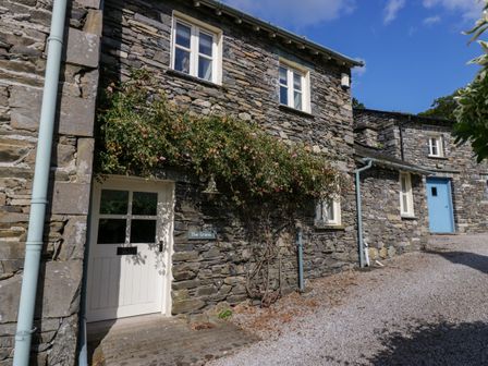 A stone exterior of a house with white and blue doors and windows with climbing plants at The Granary in Hawkshead