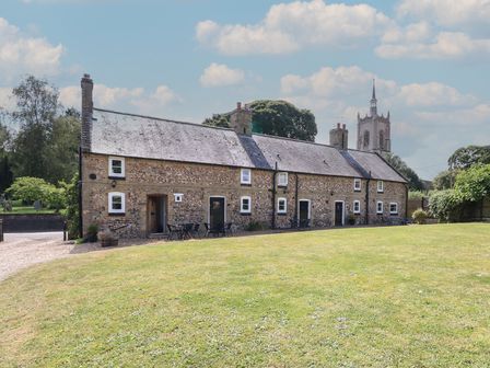 A stone cottage with multiple doors and windows behind a grassy lawn at Pear Tree Cottage in Swaffham