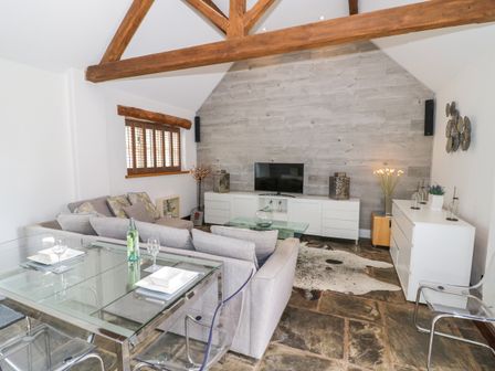 A living room with a gray sectional sofa glass dining table clear chairs and a TV on a white cabinet at The Bit on the Side in Ettington