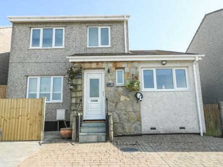 The front view of a two-story house with multiple windows a white door stone and pebble dash exterior and a driveway at Ty Copr in Amlwch