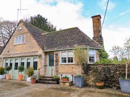 A stone cottage with a slate roof and multiple potted plants outside at The Elm Coach House in Chipping Norton