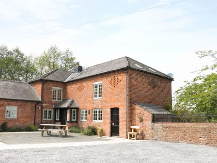 A brick house with multiple windows and a wooden picnic table outside at Garden Cottage in Kerry