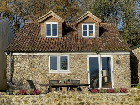 A stone house with two dormer windows a patio table and chairs in front at The Wheelhouse in Beacon near Yarcombe