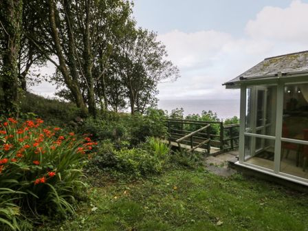 A garden with orange flowers trees and a wooden walkway next to a glass room at Woodland Roost in Barmouth