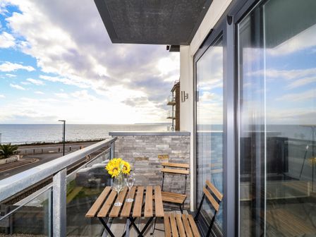 A balcony with a small wooden table and two chairs overlooking the sea at 7 Warren Edge Close in Bournemouth