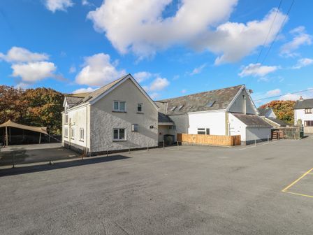 A large white building with multiple windows and a paved parking area under a blue sky at Glyntawe Outdoor Centre in Penycae near Ynyswen