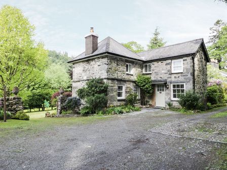 A stone house with a slate roof surrounded by trees and shrubs at Beaver Grove Cottage in Betws-Y-Coed